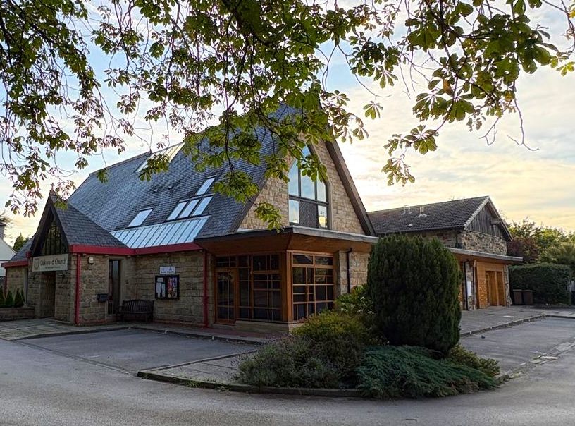 Oakwood Church on Springwood Road from the car park, a stone building with a steep slate roof and glazed wooden entrance, framed by chestnut branches overhead
